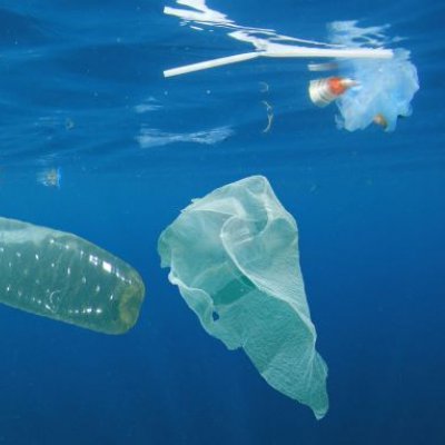 a bottle, plastic bag and straw float in blue water